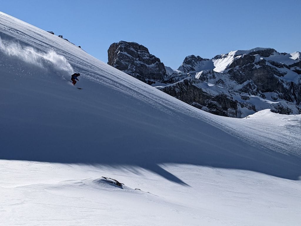 A skier spraying some pow, offpiste, in front of a blue sky