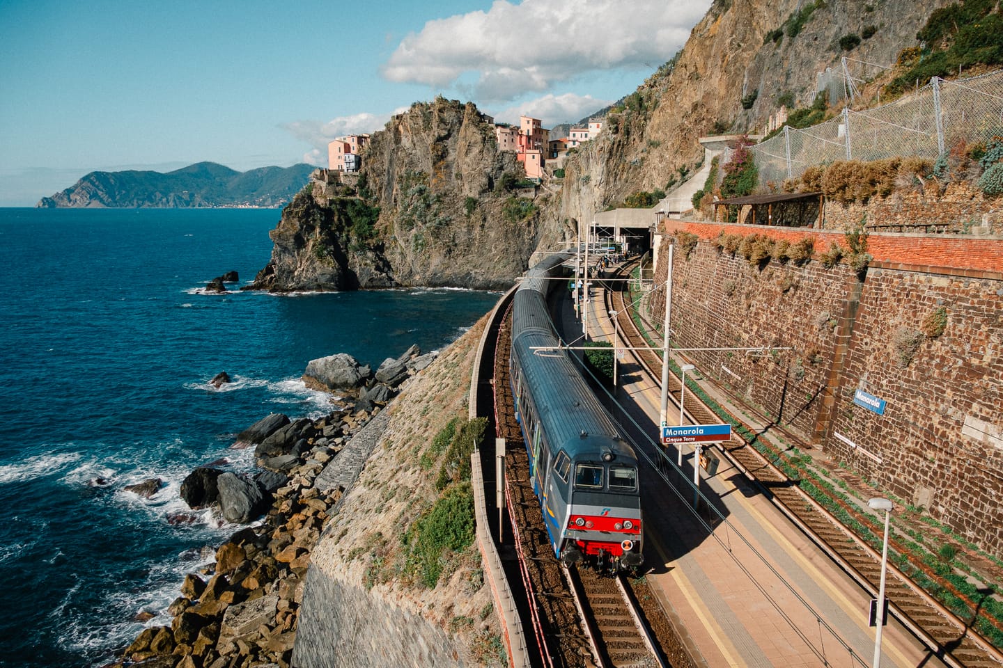Ein Zug fährt der ligurischen Küste entlang, im Hintergrund Dörfer der Cinque Terre